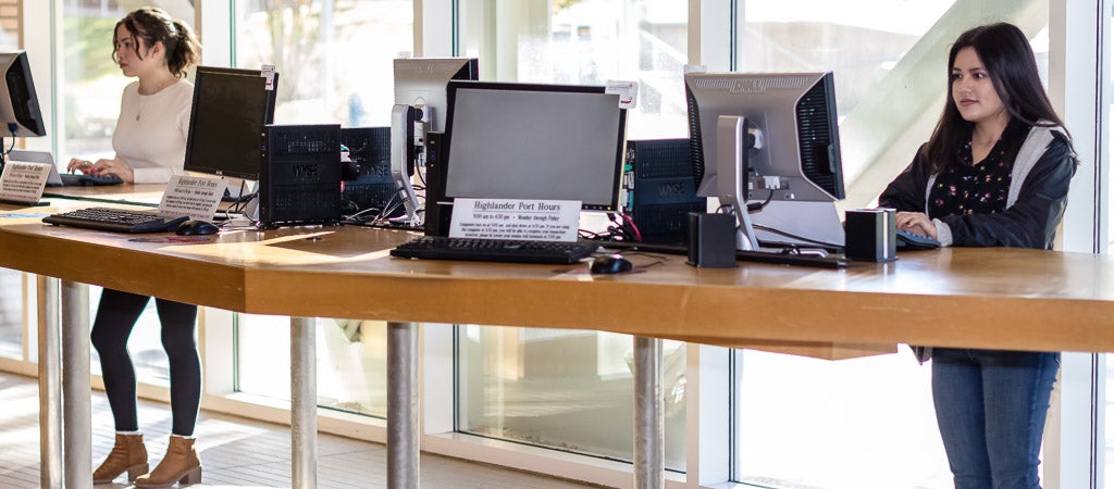 Two UCR students use the workstations in the Highlander One-Stop Shop (HOSS).