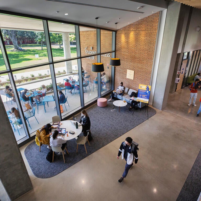 Students walk through a building that has floor to ceiling windows.
