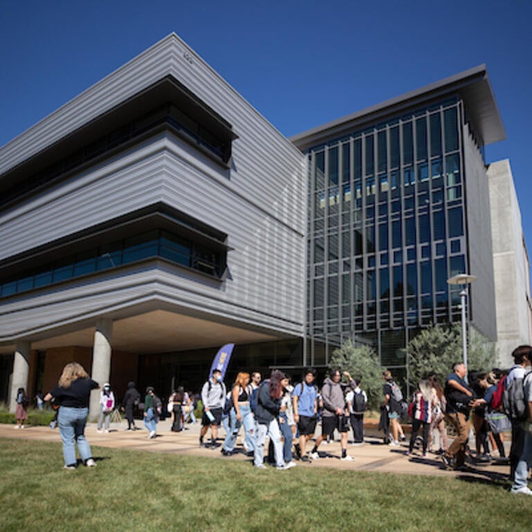 A large group of students walk outside of the Student Success Center, a very industrial looking building.