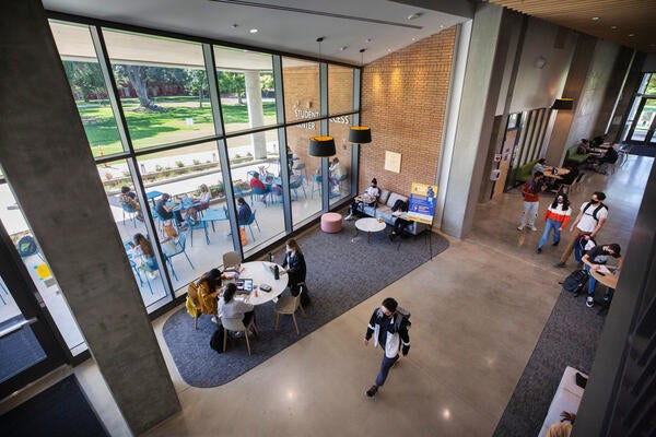 Students walk through a building that has floor to ceiling windows.