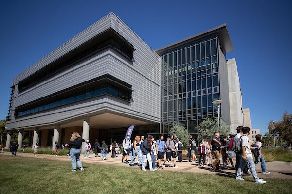 A large group of students walk outside of the Student Success Center, a very industrial looking building.