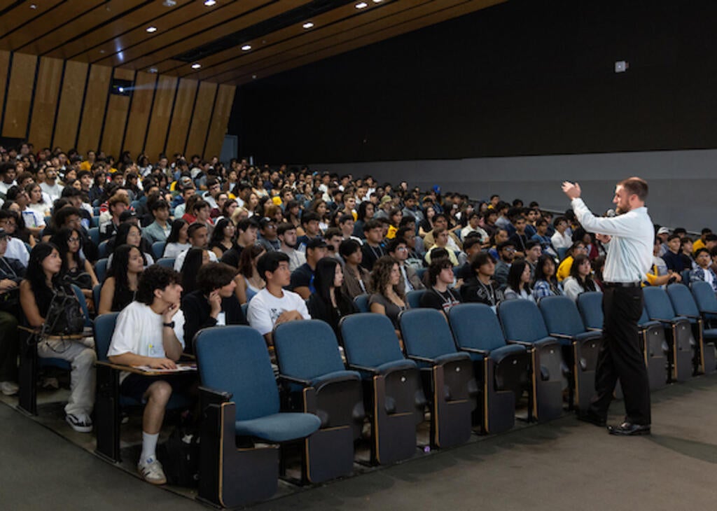 A large lecture hall with students in seats and a lecturer at the front of the room.